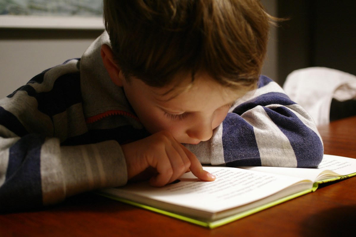 A child follows the words in an open book at a wooden table