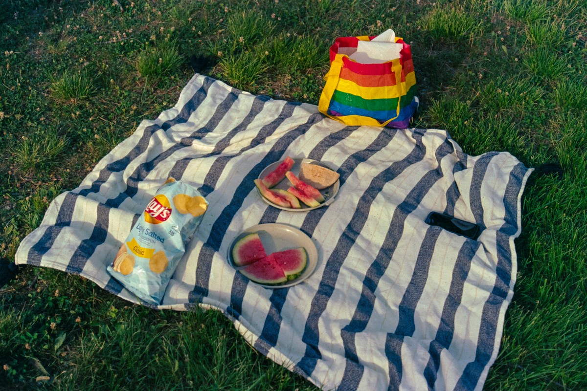 Watermelon and snacks on a striped picnic blanket in the grass